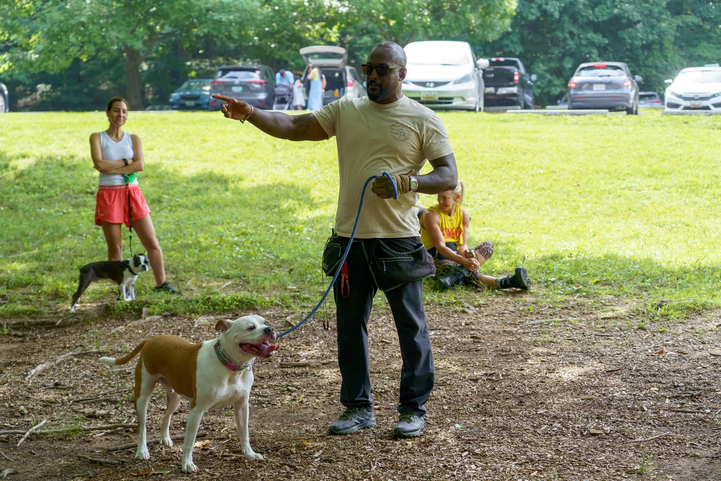 Jay giving a hand signal on an open field, directing a tan and white bulldog on lead while a handler looks on.